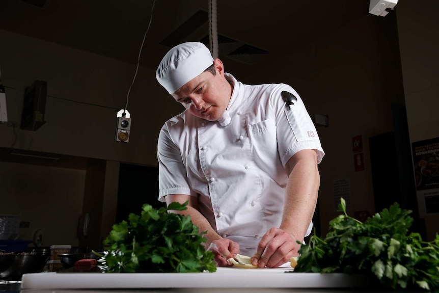 A man wearing a cook's outfit cutting up vegetables