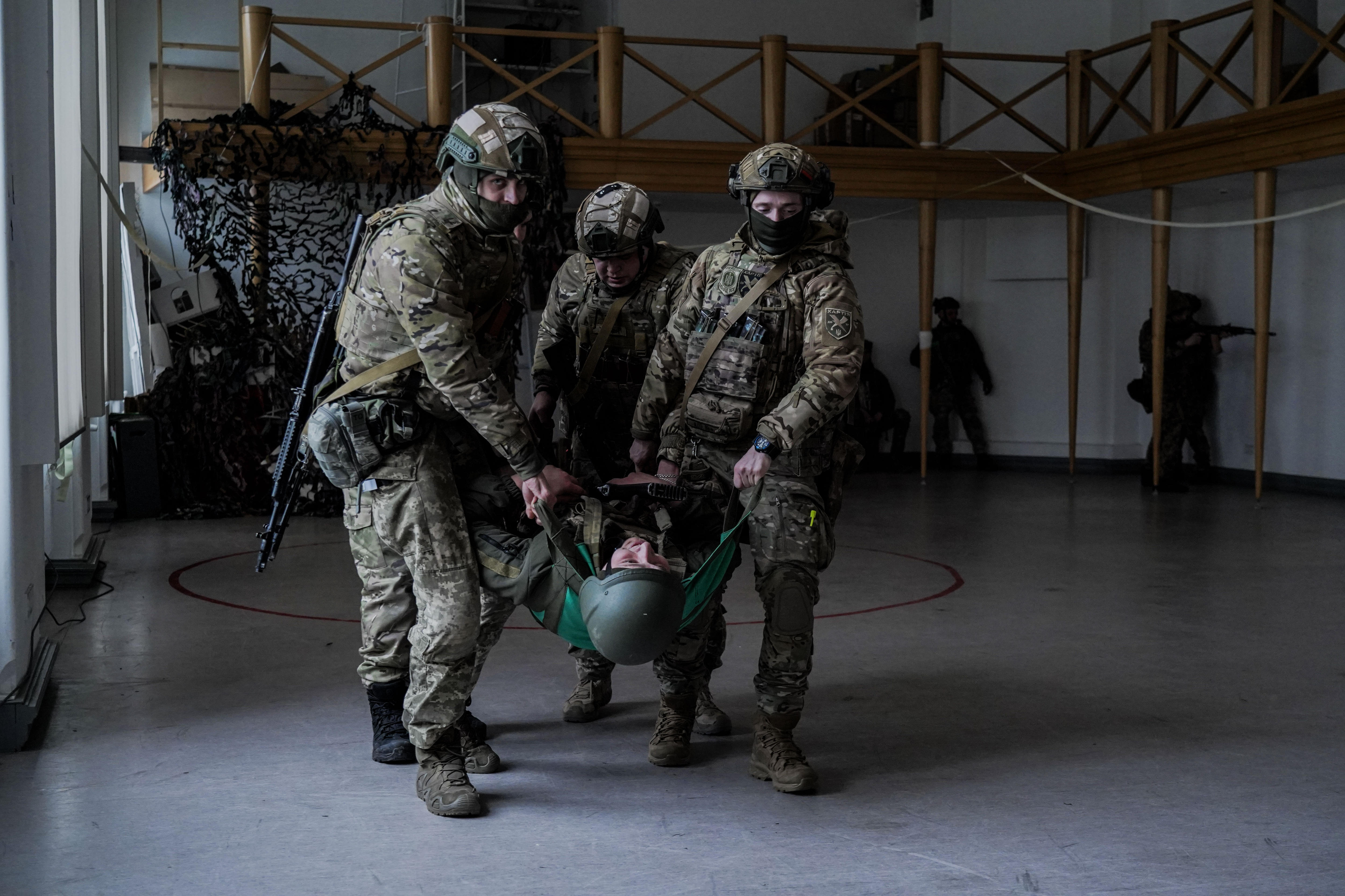 Three men in combat gear carry a man in a helmet through a warehouse