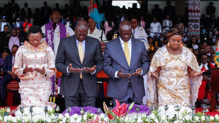 william ruto, Rigathi Gachagua and their wives kneeling in prayer in colourful hall with flowers in front