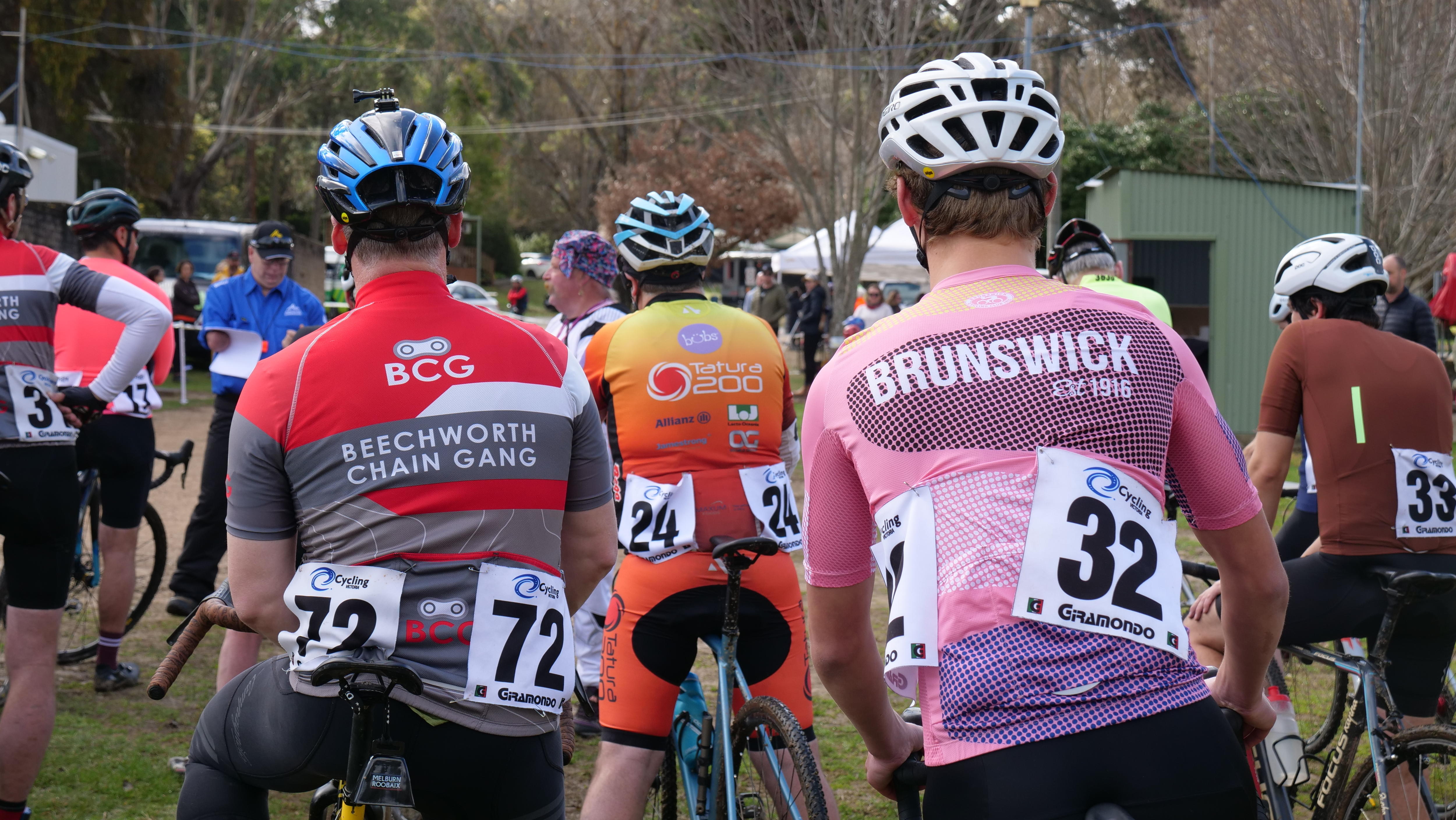 A shot of the backs of riders about to race.  They are wearing a range of jerseys from Beechworth, Tatura and Brunswick.