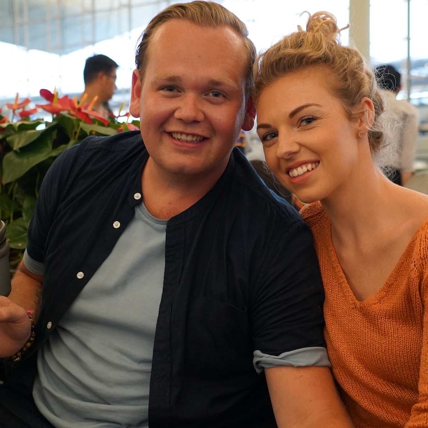 A mand and woman smile while they are seated in an airport