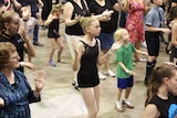 A young girl with her hands in the air watches the instructors as she participates in a tap dancing lesson.