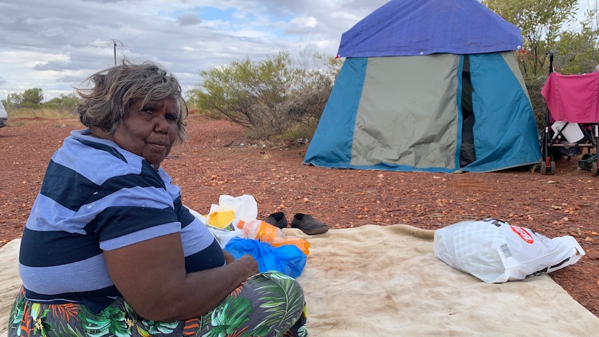 Bonnie Camphoo sits on the ground with her tent in the background.