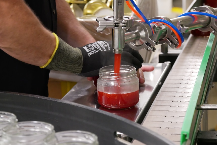 A pump is pours red liquid into a glass jar.