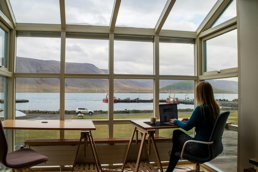 Lady sitting at a desk on her laptop with a view overlooking a lake