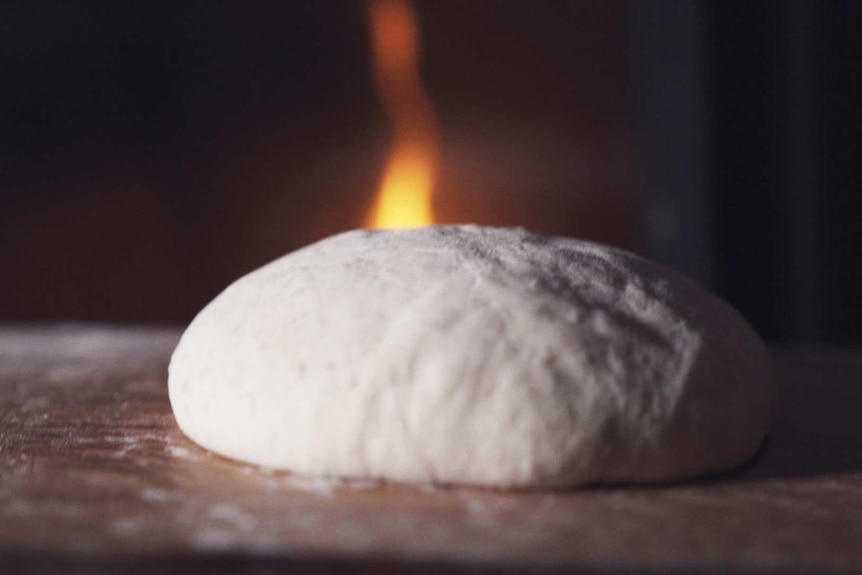 A raw sourdough loaf in front of a flame.