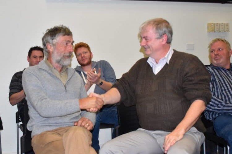 Two men in smart casual wear sitting down, shaking hands.