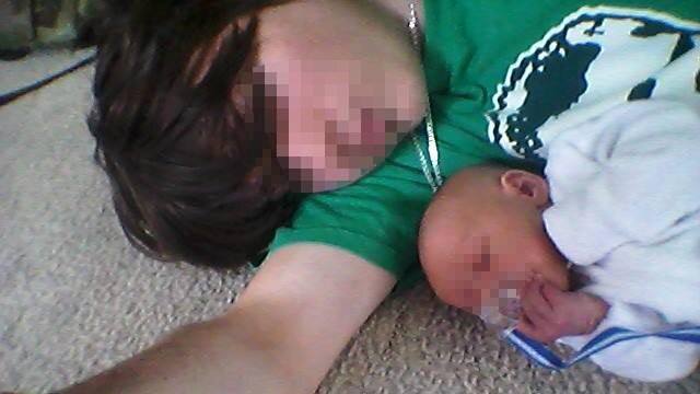 Man lying on the floor with his baby son, both with faces pixellated.