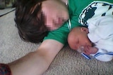 Man lying on the floor with his baby son, both with faces pixellated.