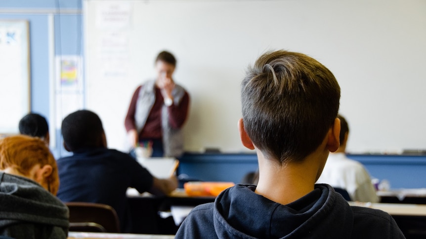 A boy faces a teacher who is standing in front of a blackboard.