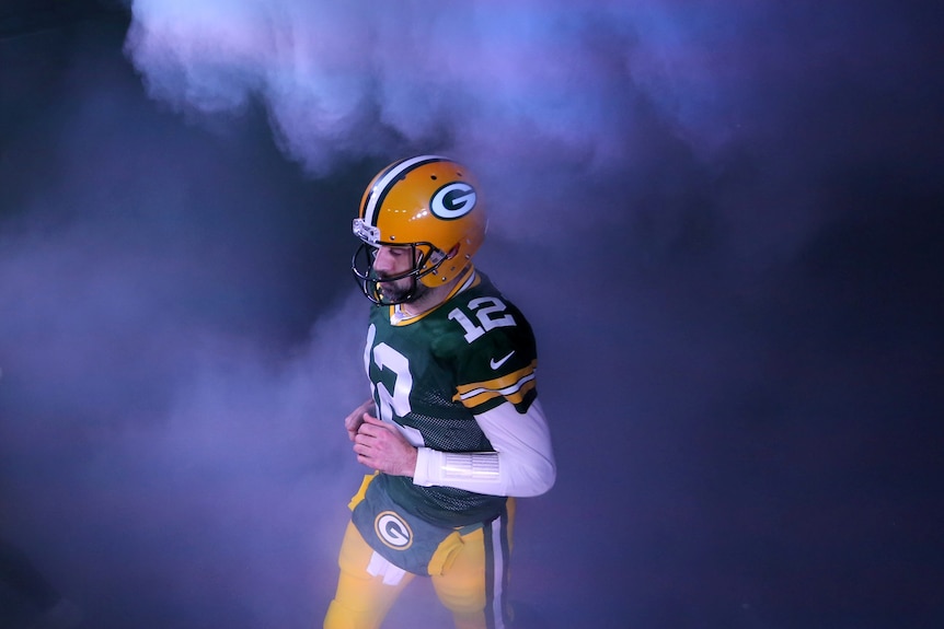 Aaron Rodgers in a football helmet and uniform running through billowing mist
