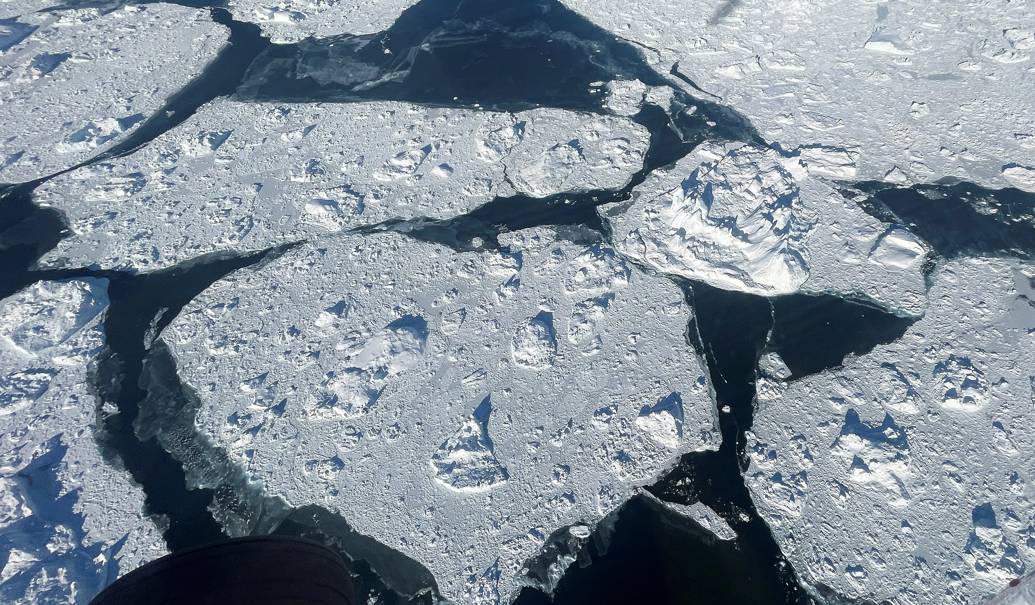 Aerial photo of sheets of ice cracked and floating on water 