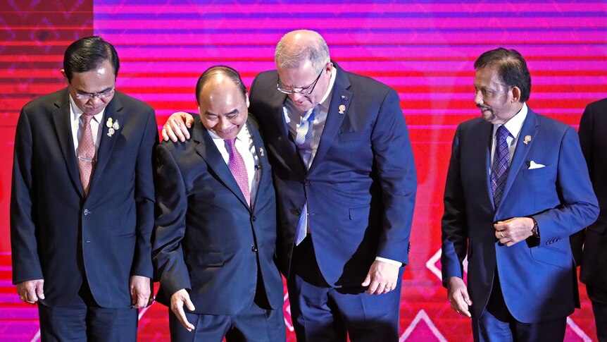 Scott Morrison hugs Vietnam's Prime Minister Nguyen Xuan Phuc in front of a pink and purple background.