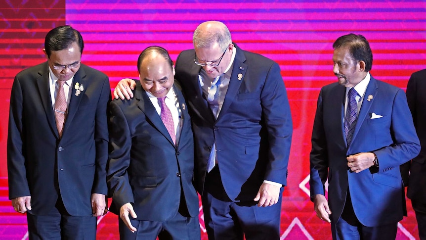 Scott Morrison hugs Vietnam's Prime Minister Nguyen Xuan Phuc in front of a pink and purple background.