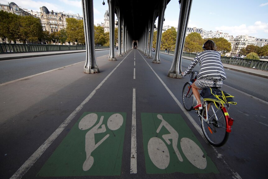 A cyclist on a bike path under a bridge in a European city