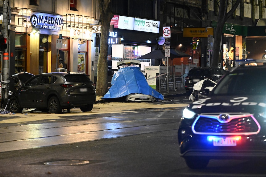 The lights of a police car flash in the foreground of a photo of a car crash