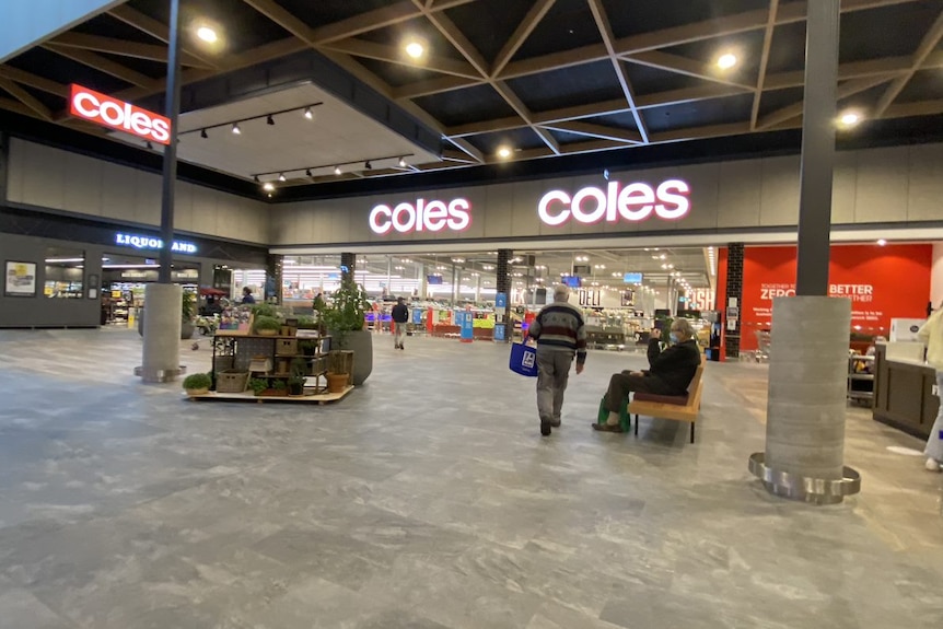 A wide view of the entrance to a large Cole supermarket with two unidentifiable people outside.