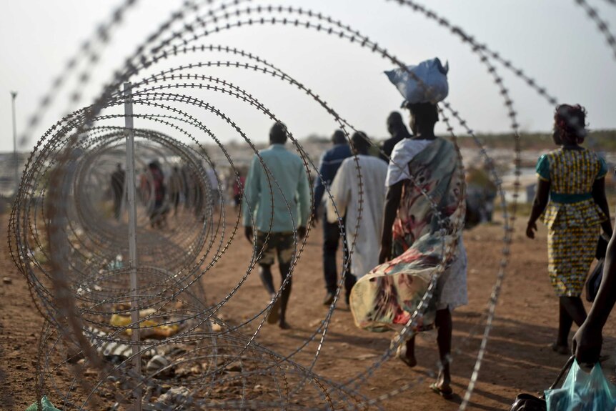 Displaced people walk next to a razor wire fence at a UN base.