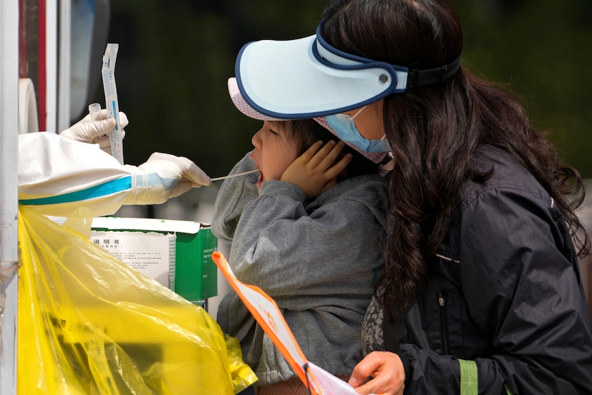 A woman lifts her child to get a COVID-19 test at a private mobile coronavirus testing facility.