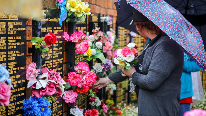 A woman holds a bouquet of flowers at the memorial wall.
