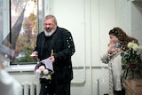 Colleagues spray champagne toward Dmitry Muratov who smiles while holding a bunch of flowers.