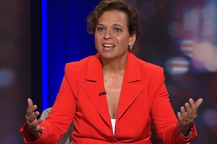 A woman wearing a red suit gesticulates with her hands.