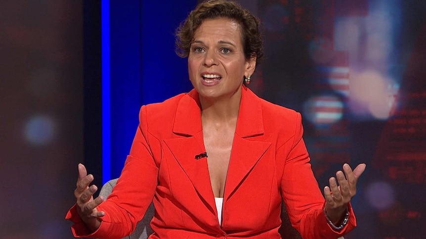 A woman wearing a red suit gesticulates with her hands.