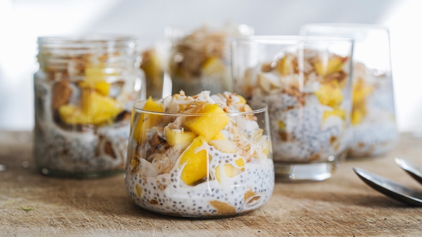 Five jars and glasses filled with mango, coconut and ginger trifle, an easy Christmas dessert that can be vegan.