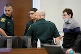 Three male court officers escort a young male murderer from a courtroom.