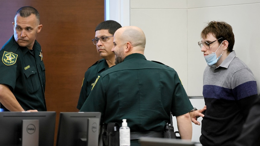 Three male court officers escort a young male murderer from a courtroom.