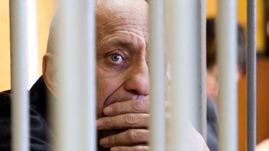 A man with his hand on his mouth, obscured by prison bars.