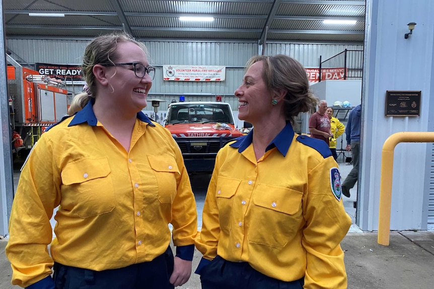 A mother and daughter stand next to each other in uniform, laughing