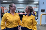 A mother and daughter stand next to each other in uniform, laughing