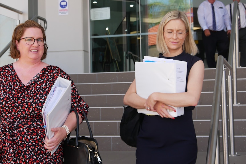 Two women walking out of court with files in hand, one has brown short hair, the other has blonde short hair