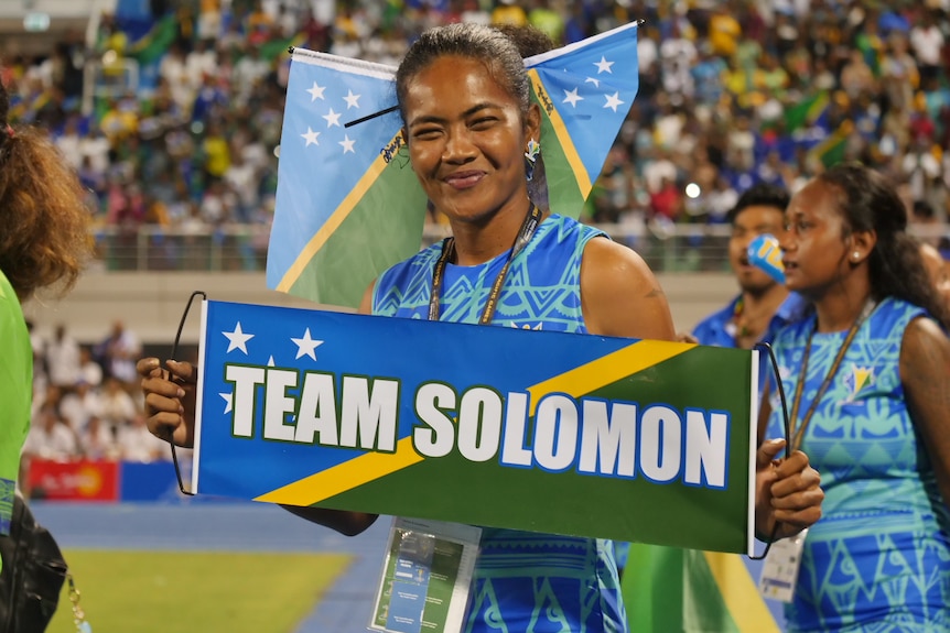 A smiling woman holds up a sign saying Solomon as she walks on the field at then opening ceremony.