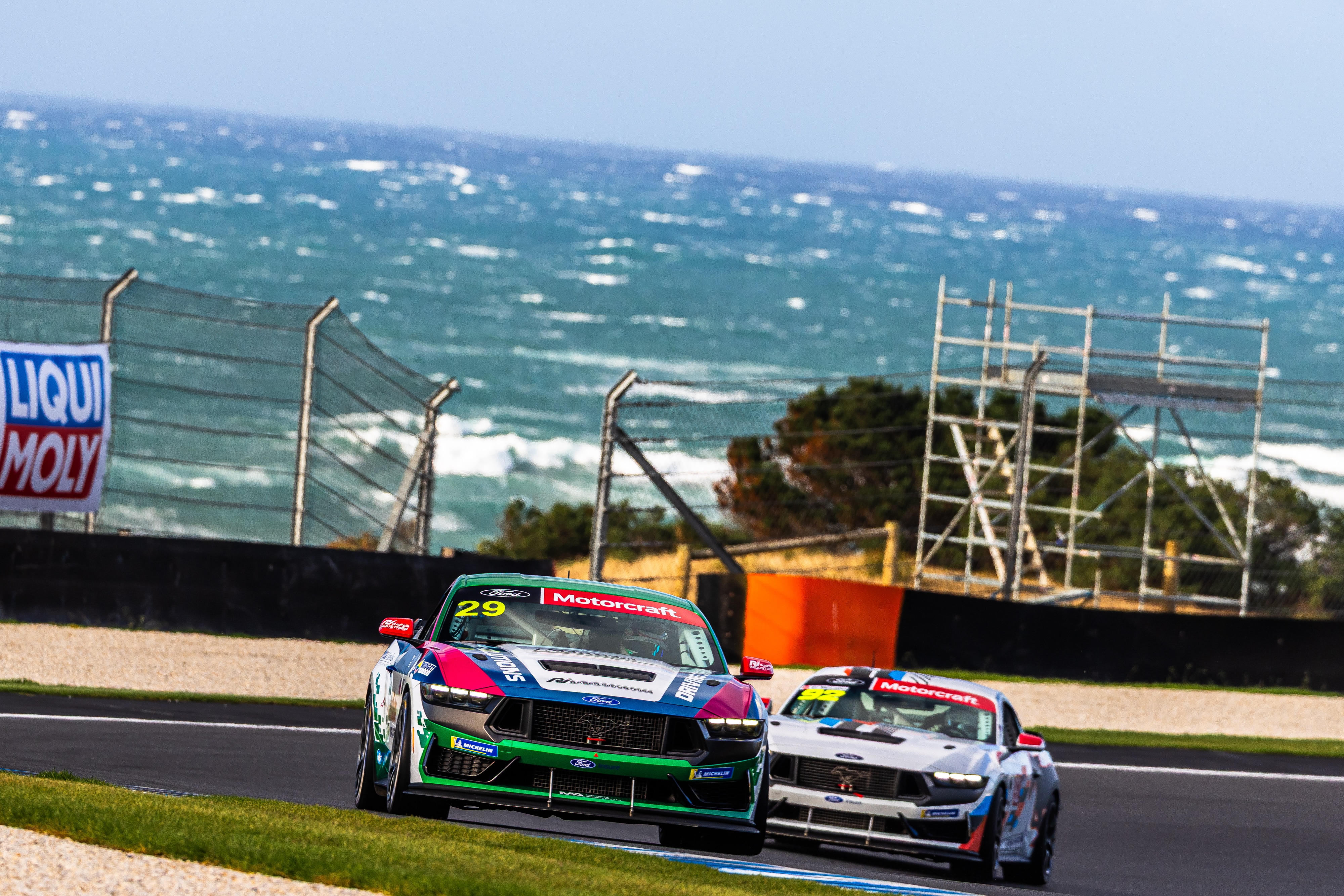 Dois carros de corrida fazem uma curva com um oceano agitado atrás deles.
