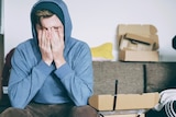 Man in a hoodie sitting on a couch with his hands over his eyes