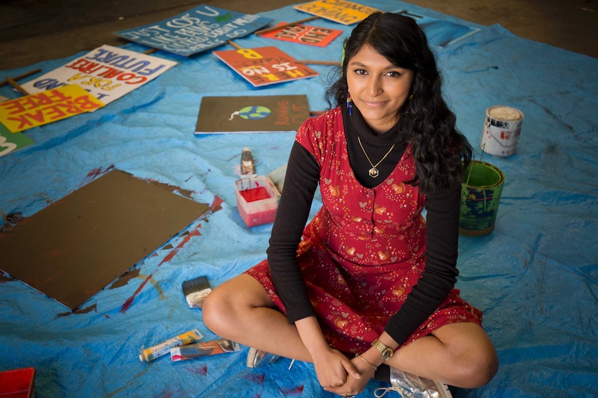 A young girl in a red dress sitting on the ground, surrounded by placards with climate protest slogans.