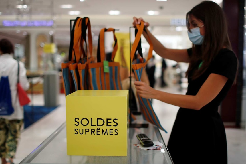 An employee, wearing a protective face mask, checks bags with discount signs at a department store
