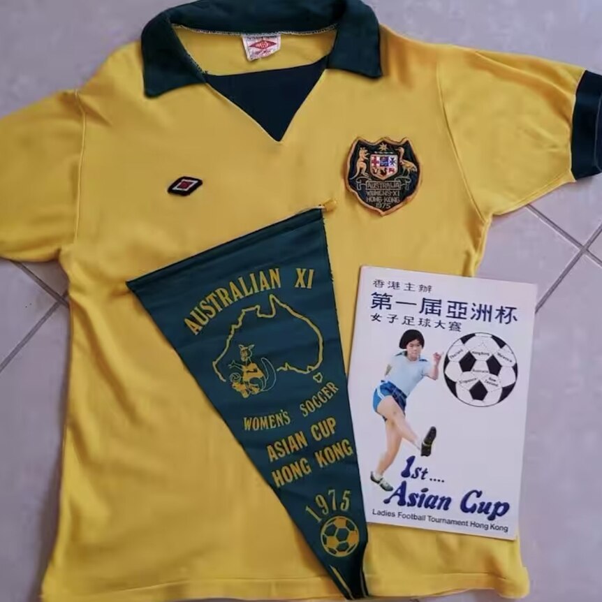 A yellow and green soccer jersey with the Australian coat of arms, a green flag, and a match day program for a tournament