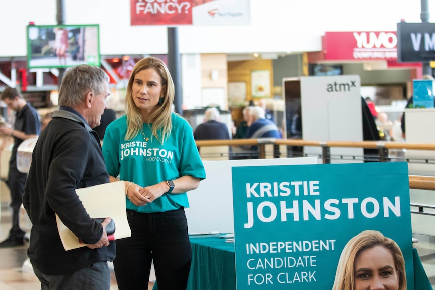 A woman in a green t-shirt speaks with an older man in a shopping centre