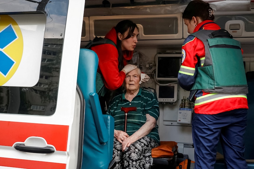 An elderly woman in the back of an ambulance as two paramedics lean over the top of her 