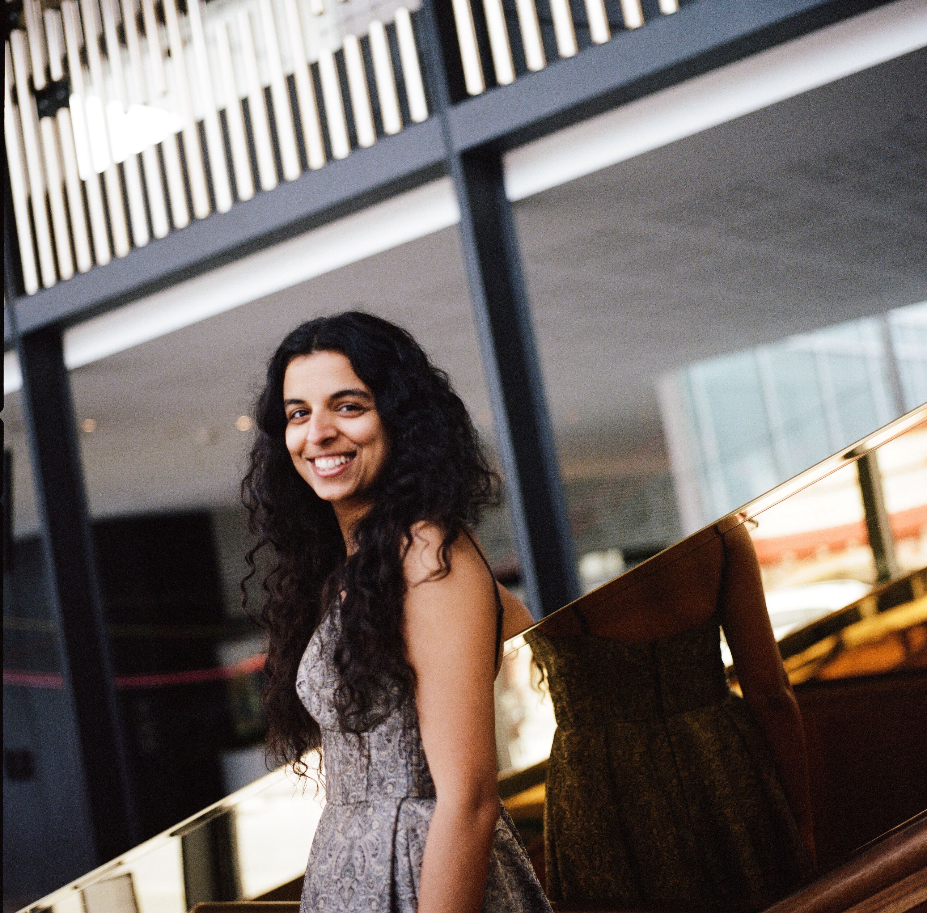 Uma mulher australiana do sul da Ásia, na casa dos 30 anos, posa em uma escada, vira a cabeça para o lado e sorri.