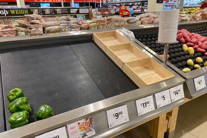 Produce aisle in supermarket looking bare, with a few lonely capsicums and potatoes.