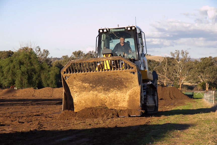 A bulldozer scraping earth on a paddock block with piles of dirt in the background