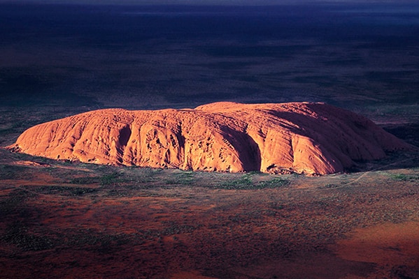 Uluru is highlighted as the sun hits it in the early morning.