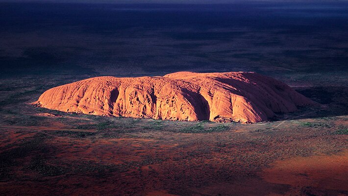 Uluru is highlighted as the sun hits it in the early morning.