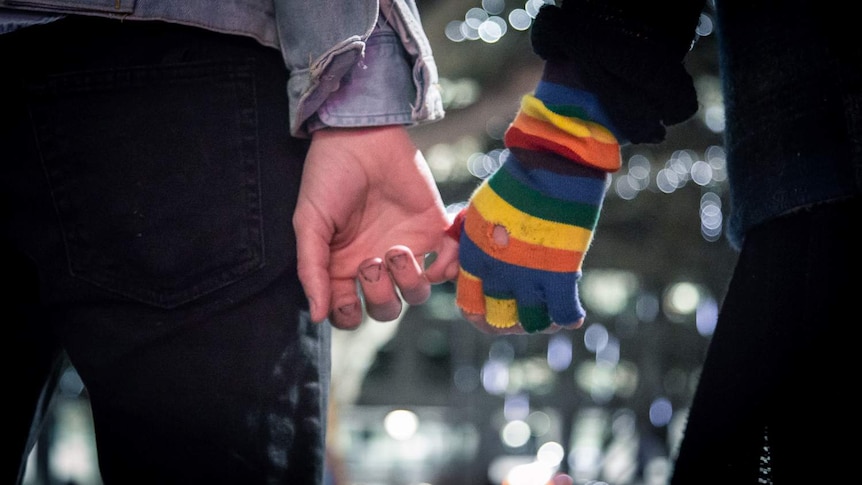 A man and a woman are holding hands on the street at night.