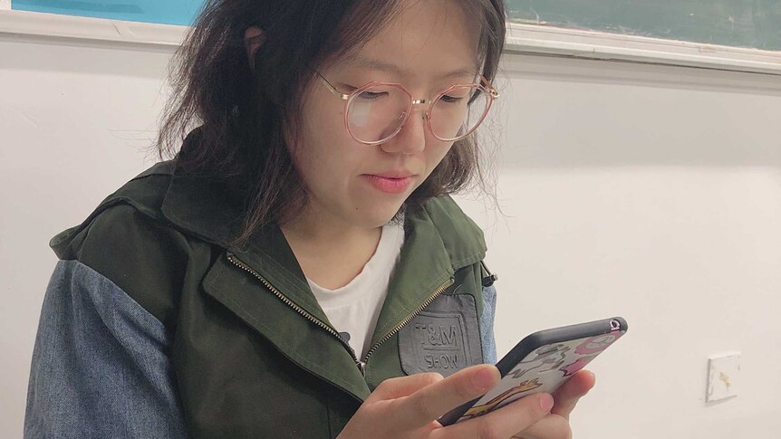 A young Chinese student using mobile phone in the classroom.