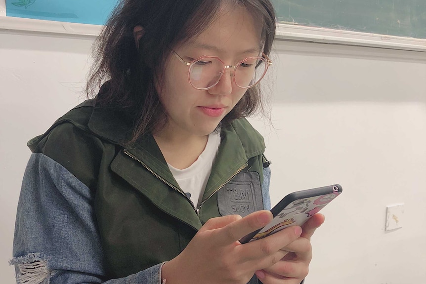 A young Chinese student using mobile phone in the classroom.